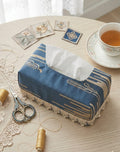 Blue tissue box cover on a table with a cup of tea and decorative items.
