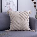 Textured pillow with tassels on a gray sofa, with a framed picture of a deer in the background.