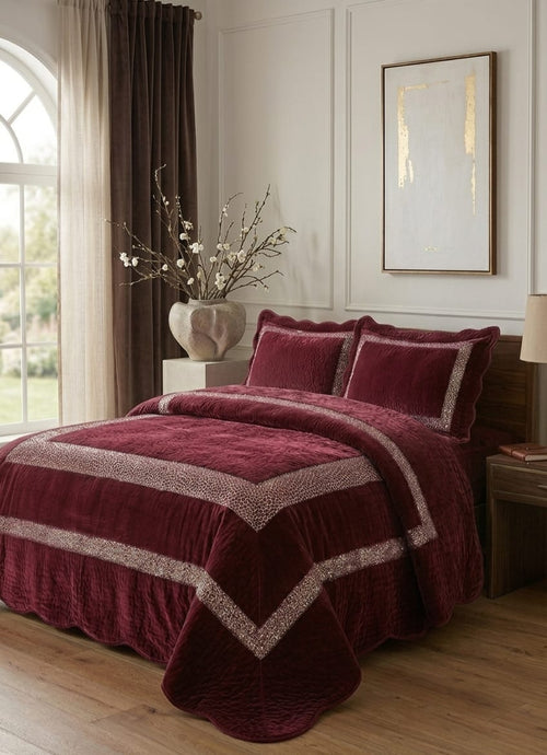 Maroon bedspread with decorative pillows in a bedroom setting.