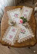 Decorative table setting with lace placemats, teacup, and flowers on a wooden table.
